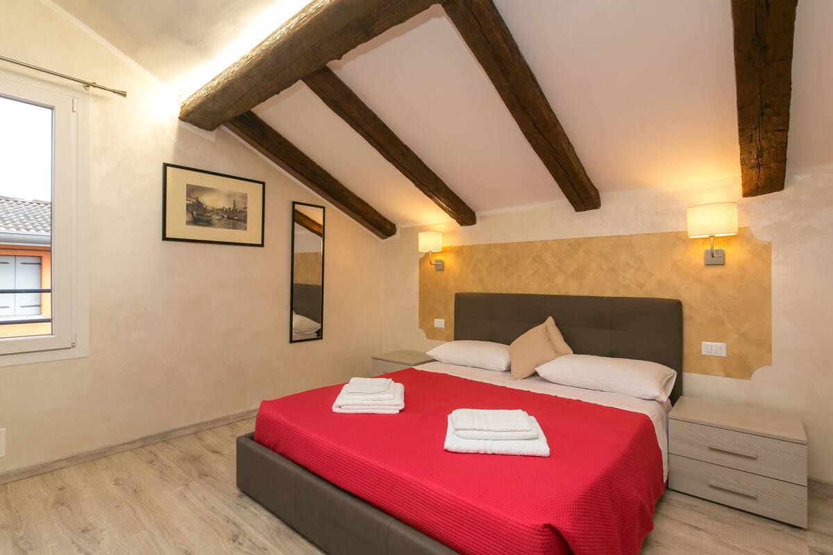 A bedroom with a bed, bedside tables, a mirror, and a picture on the wall.