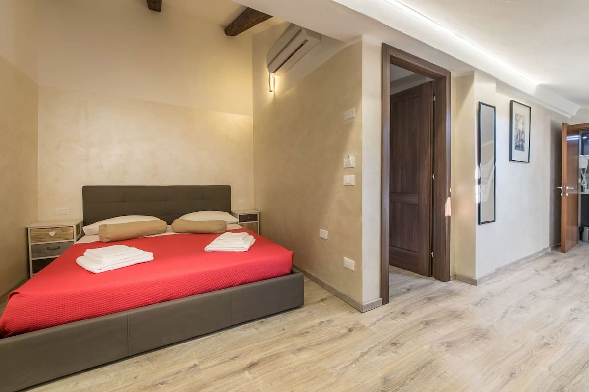 A bedroom with a bed, bedside tables, and a door leading to another room.