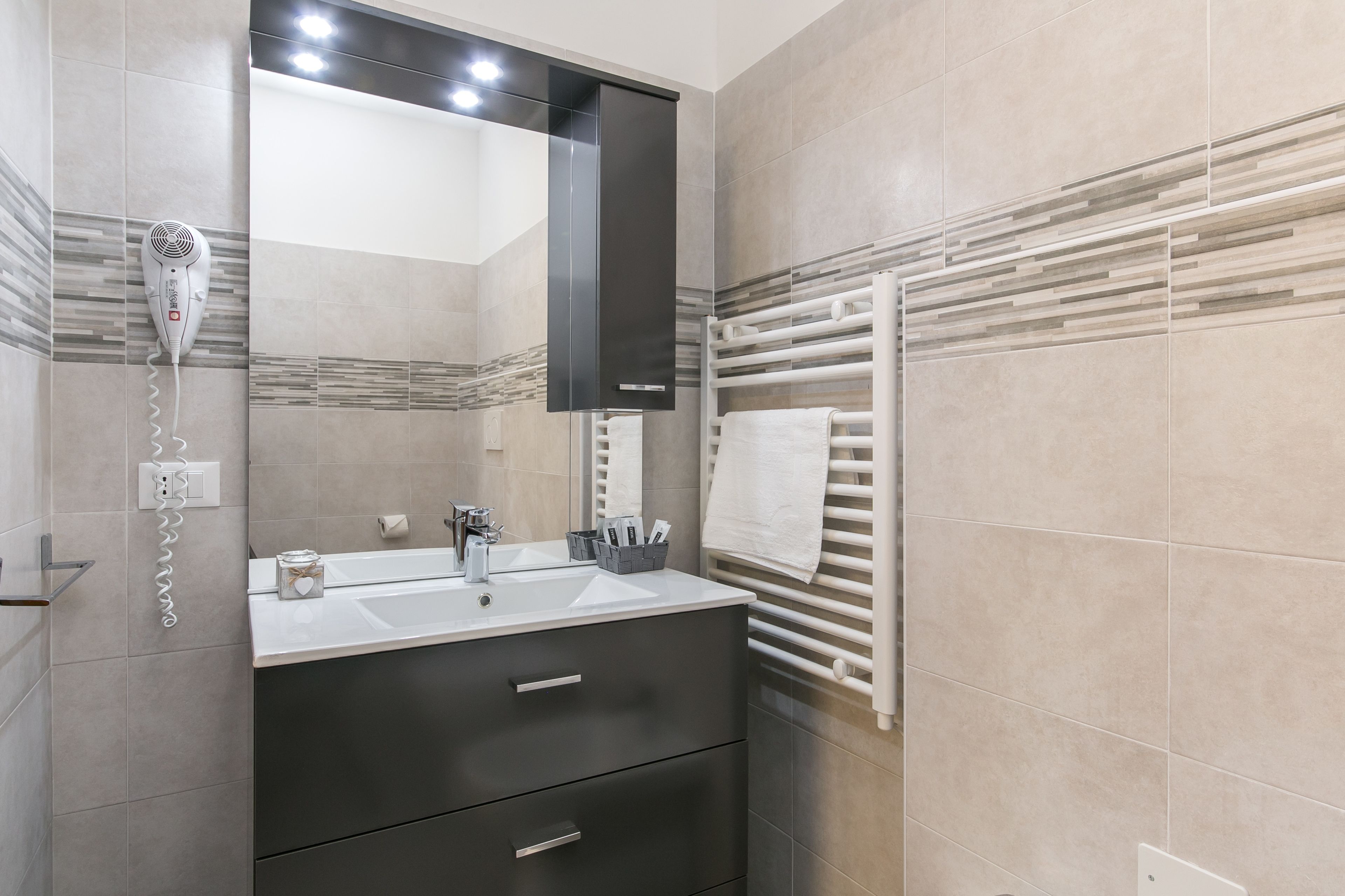 Un baño moderno con un espejo grande, un secador de pelo, un perchero para toallas y un lavabo con un mueble oscuro.