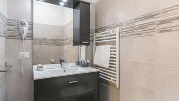 Un baño moderno con un espejo grande, un secador de pelo, un perchero para toallas y un lavabo con un mueble oscuro.