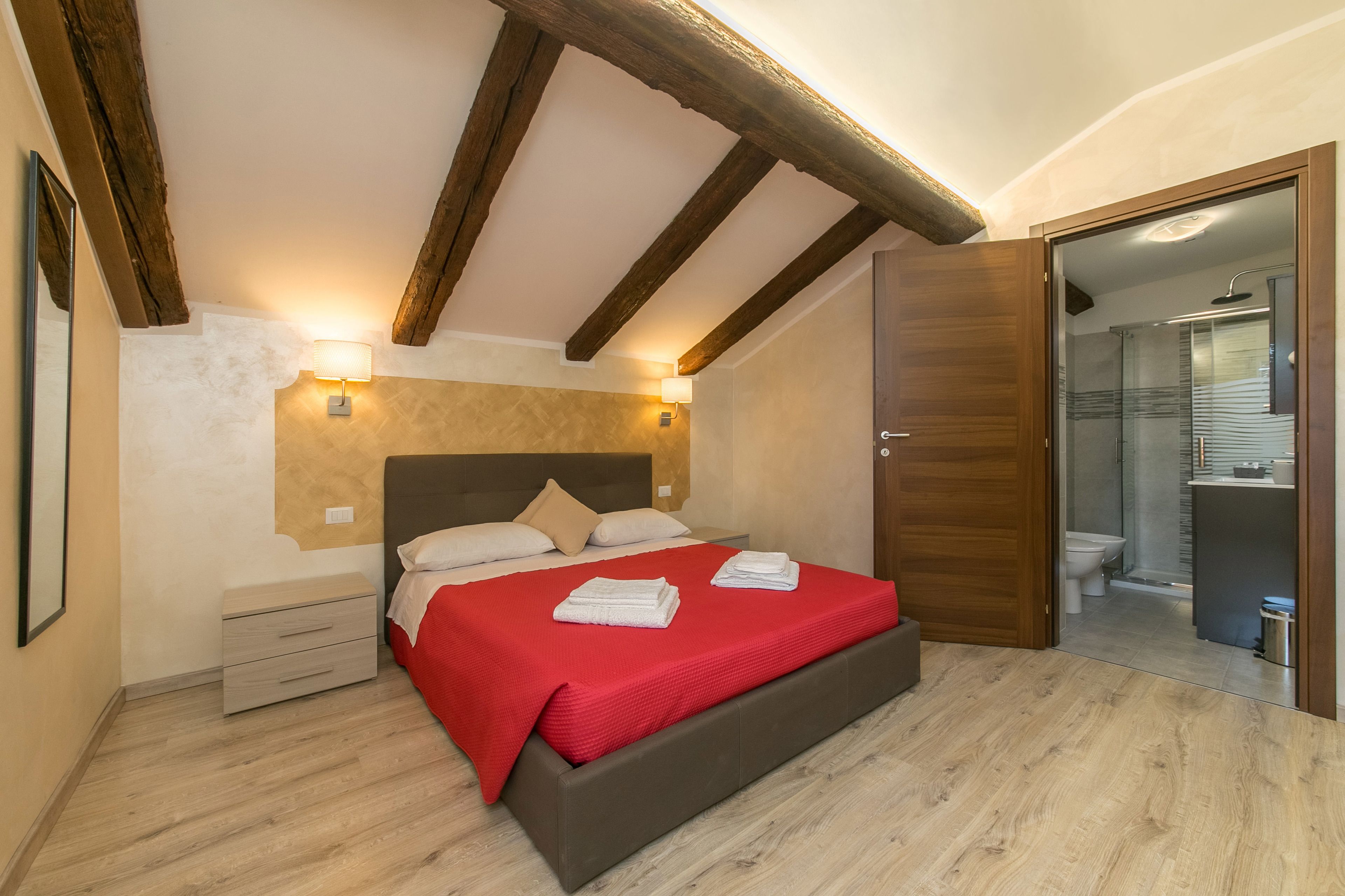A bedroom with a wooden ceiling, a bed with a red blanket, bedside lamps, and a wooden floor.
