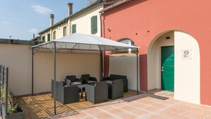 A covered outdoor seating area with wicker furniture, a tiled patio, and a building with a green door. - Red Lion Guest House (Mestre)