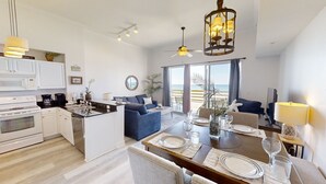 Een moderne keuken met witte kasten, een eethoek met een houten tafel gedekt voor vier personen, en een balkon met uitzicht op zee.