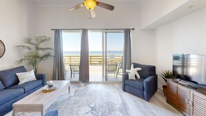 Een moderne woonkamer met een grote televisie, twee banken, een salontafel en uitzicht op het strand door de schuifdeuren.