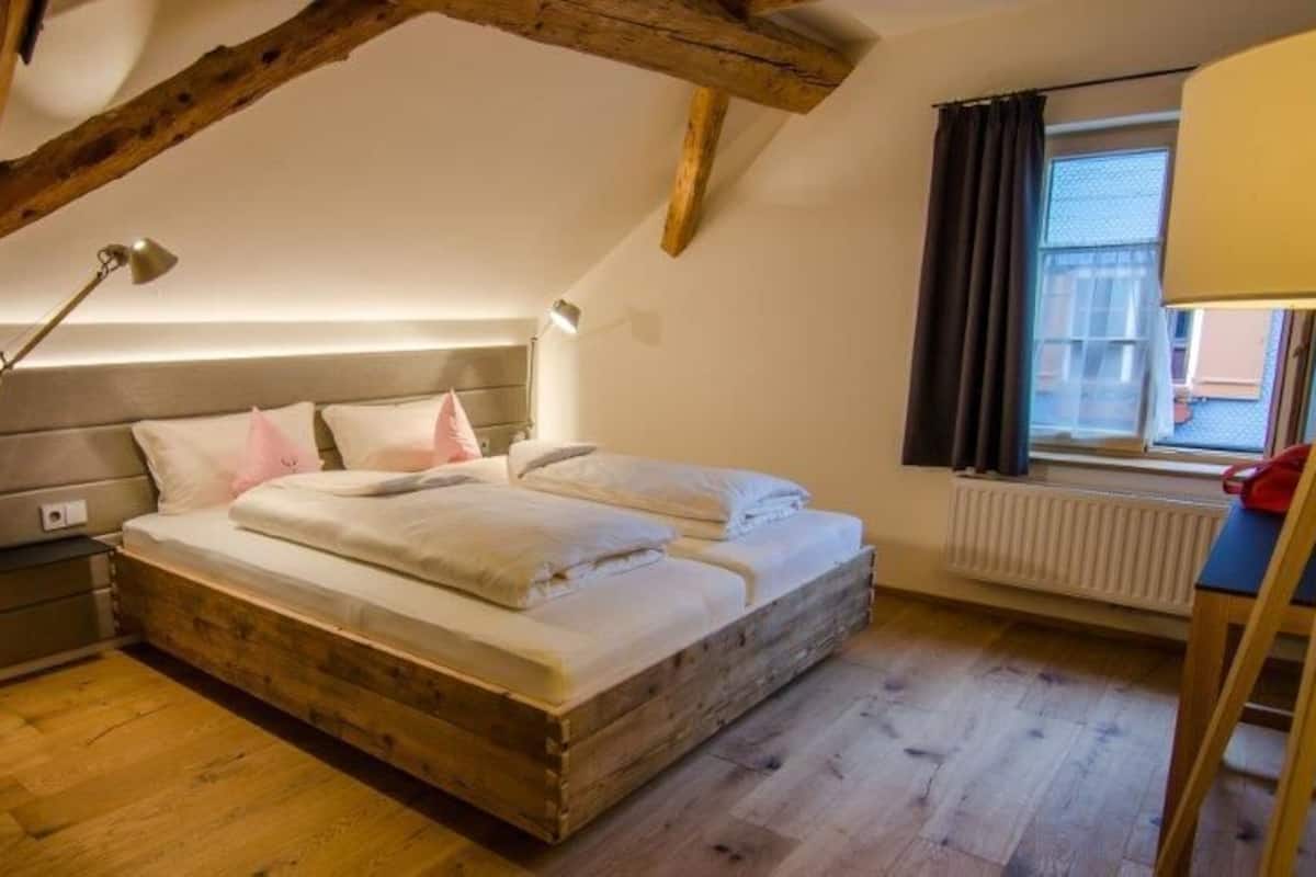 A bedroom with a wooden bed, a nightstand, a lamp, and a window with curtains.