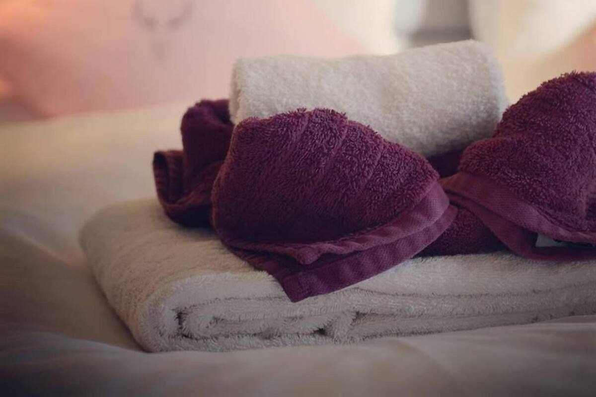 A neatly made bed with white and purple towels and a decorative pillow.