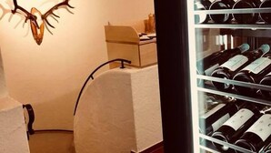 Une pièce décorée d’une tête de cerf fixée au mur, avec un lit recouvert d’une couverture blanche et un meuble à bouteilles.