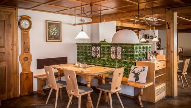 Un coin repas en bois avec une table ronde et des chaises, une horloge et un mur recouvert de carreaux verts.
