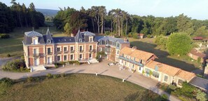 Un grand immeuble à plusieurs étages doté d’une cour intérieure, entouré d’arbres et situé dans un paysage vallonné.