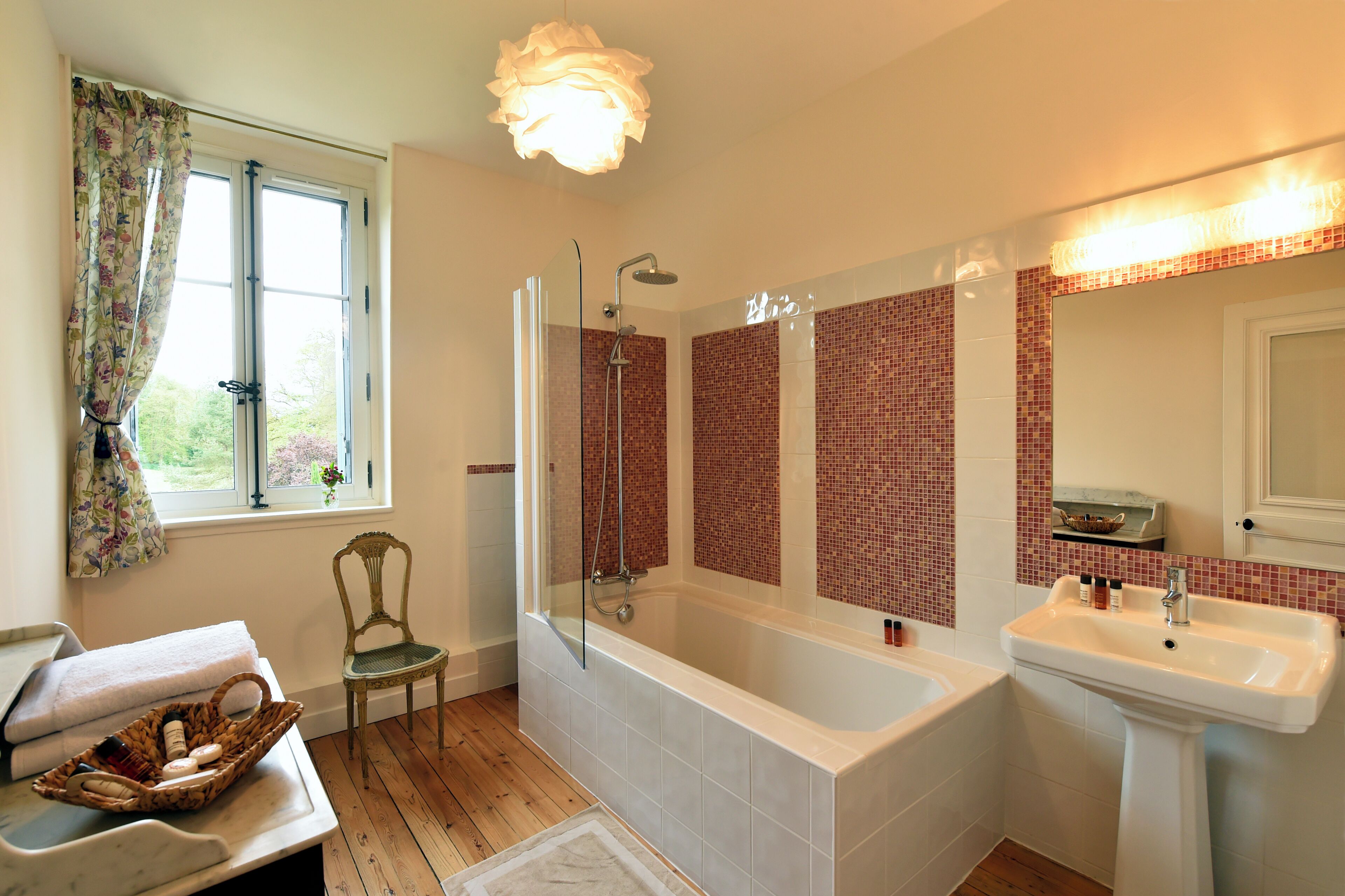 Een badkamer met een bad, een douche, een wastafel, een stoel en een raam met gordijnen.