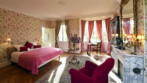 A bedroom with a large bed, a fireplace, and floral wallpaper.