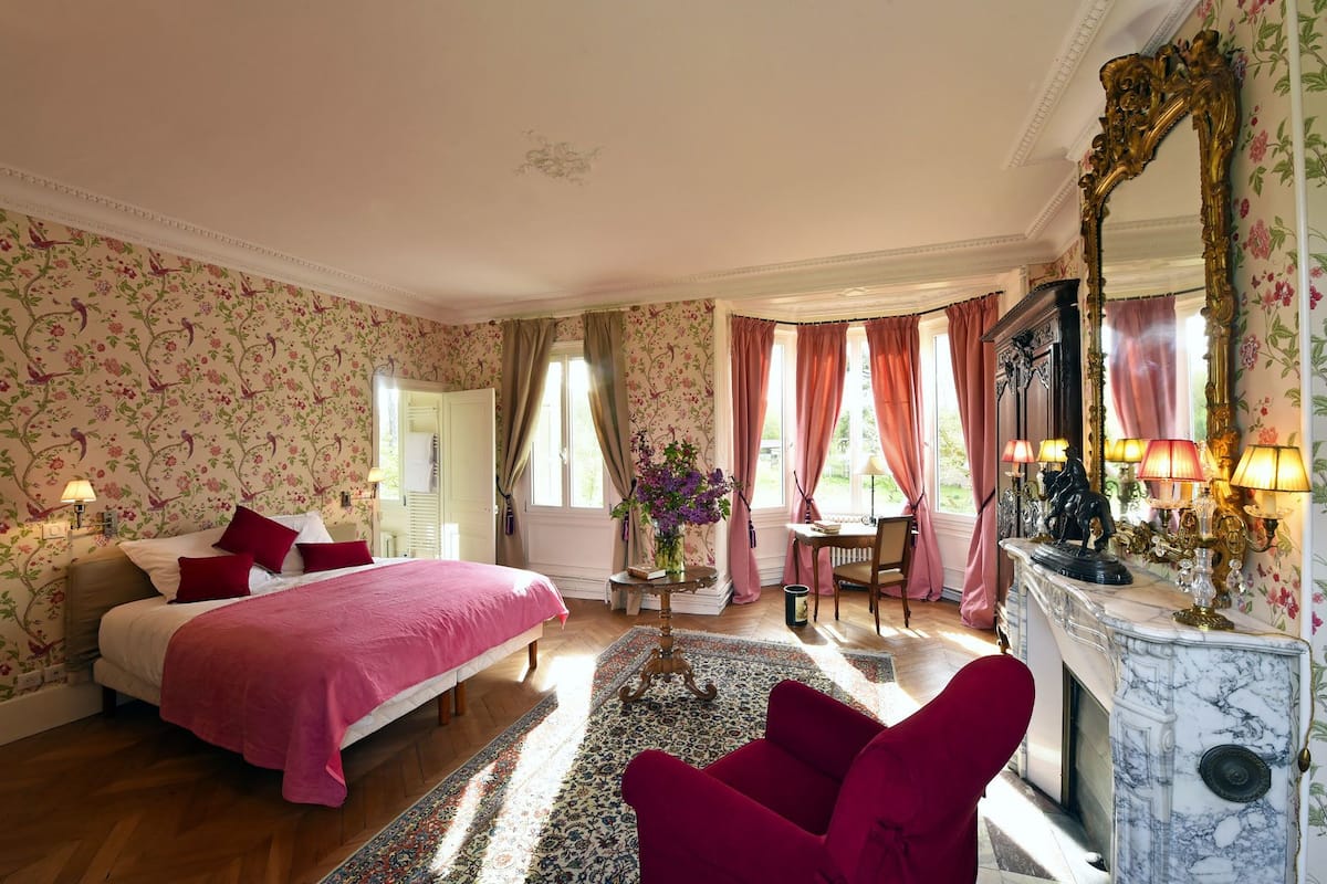 Un dormitorio con una cama grande, una chimenea y papel tapiz con motivos florales.