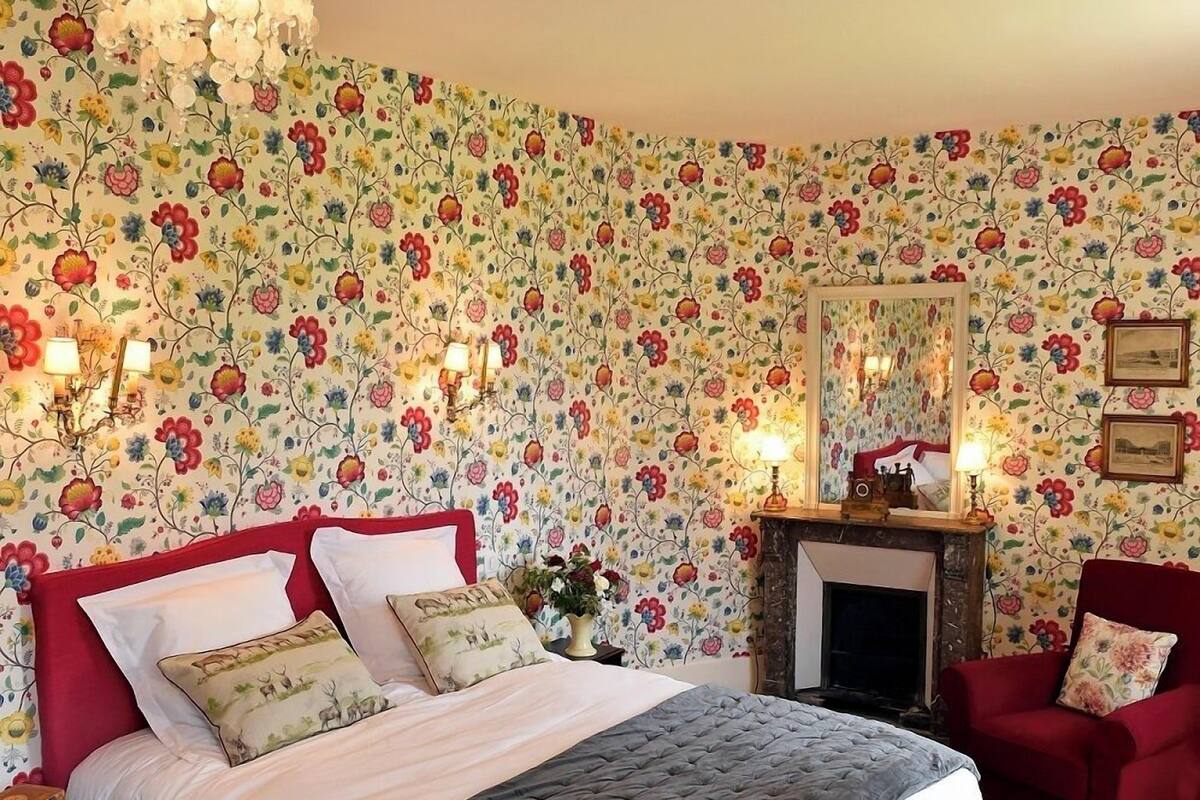 Un dormitorio con cama, candelabro, chimenea y papel tapiz floral.