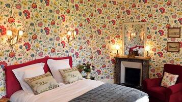 A bedroom with a bed, a chandelier, a fireplace, and floral wallpaper.