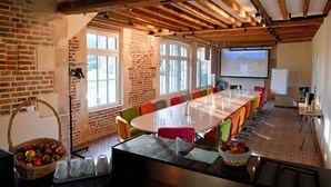 A conference room with a long table, chairs, a projector screen, and a brick wall.