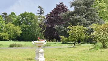 Ein Garten mit einem weißen, urnenförmigen Pflanzgefäß voller Blumen, umgeben von Gras und Bäumen.