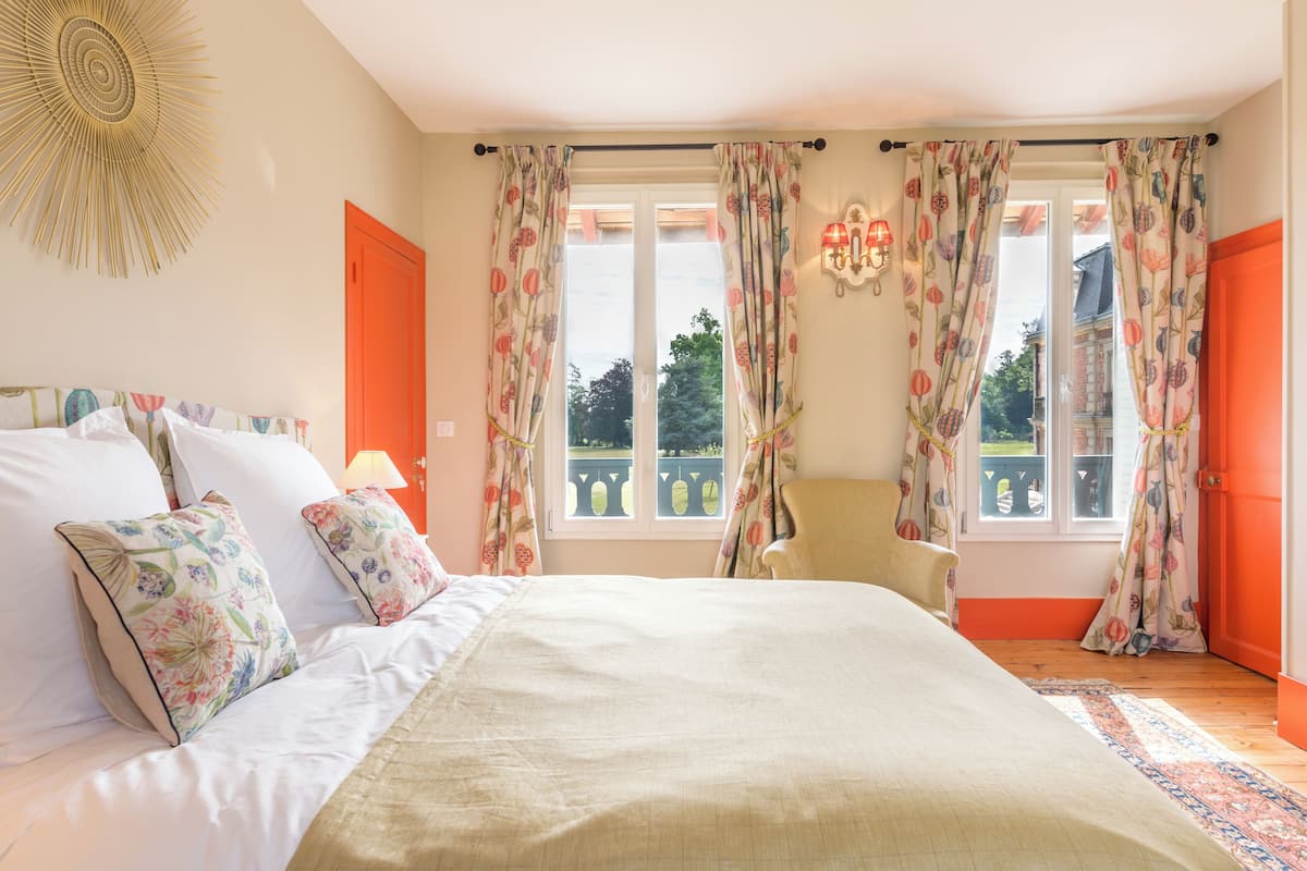 Un dormitorio con cama, cortinas, una silla y vistas al exterior.