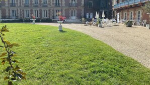 A courtyard with a lawn, outdoor seating, and a historic building with multiple windows and balconies.
