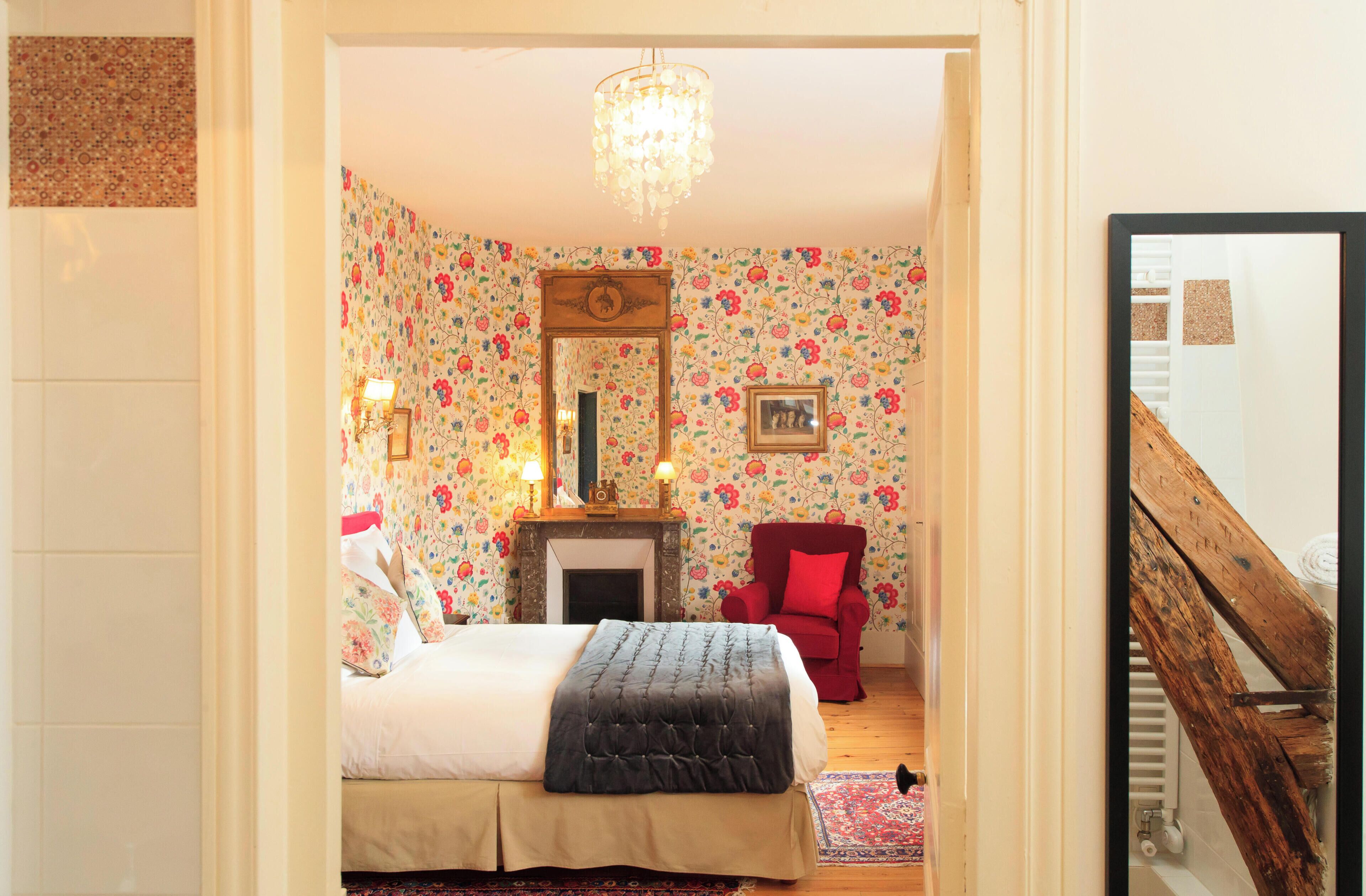 Une chambre à coucher avec un lit, un fauteuil rouge, une cheminée et un lustre.