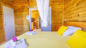 A wooden cabin room with a bed, pillows, and a bathroom visible through an open door. - New COTTAGES 300 meters walk from Grande Anse beach (ziotte)