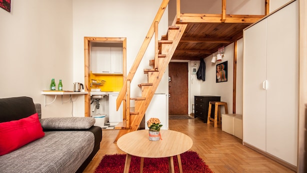 A compact living space with a sofa, a round table, a staircase, and a kitchen area. - Elegant Apartment Royal Castle (Warsaw)