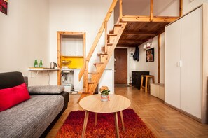 Een knus woongedeelte met een bank, een ronde tafel, een trap en een keukenhoek.