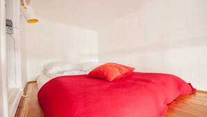 A bedroom with a wooden floor, a red bedspread, white pillows, and a single orange pillow. - Elegant Apartment Royal Castle (Warsaw)