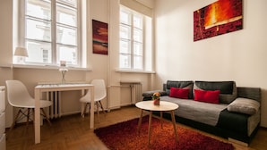 A modern living room with a grey sofa, red cushions, a small round table, and a red rug. - Elegant Apartment Royal Castle (Warsaw)