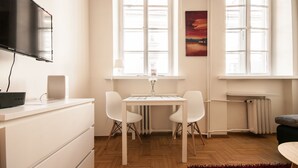 A modern, well-lit room with a wooden floor, white furniture, a flat-screen TV, and a radiator. - Elegant Apartment Royal Castle (Warsaw)