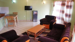 Een woonkamer met een bank, stoelen, een houten tafel, een televisie en een koelkast.