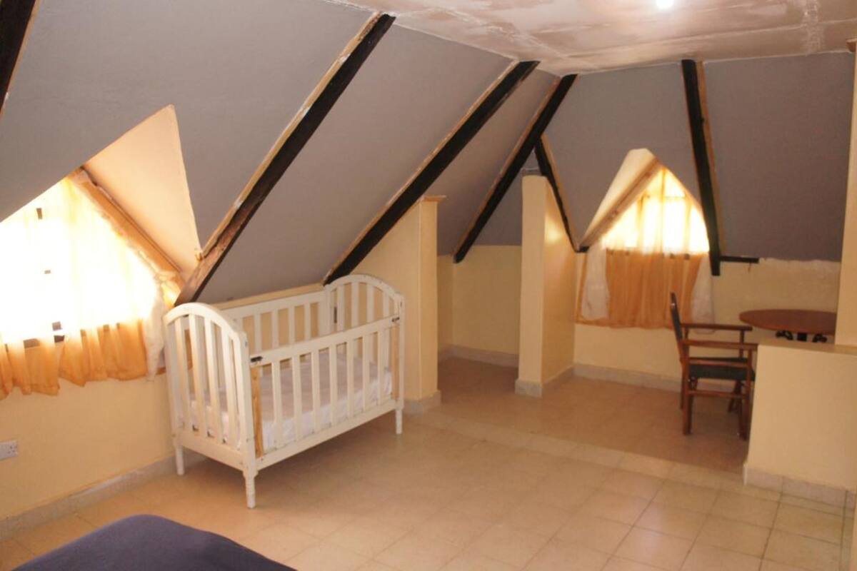 Une pièce avec un plafond en pente, un berceau blanc, une table en bois et une chaise.