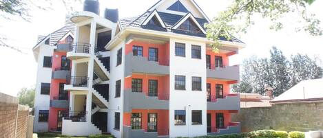 A multi-story residential building with a central staircase, balconies, and a well-maintained lawn.