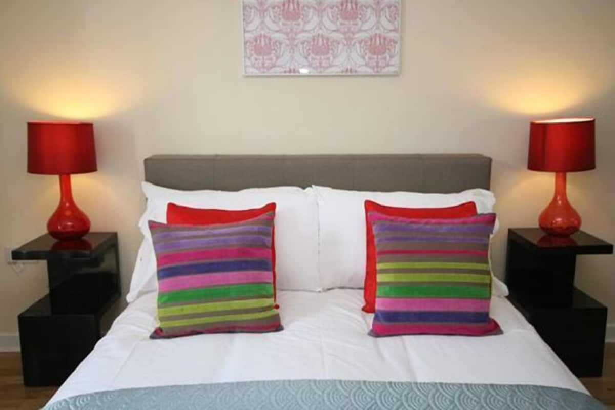 A bed with white bedding, two striped pillows, and red lamps on black nightstands.