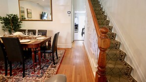 A dining area with a wooden table set for four, a large mirror above, and a staircase with patterned carpet.