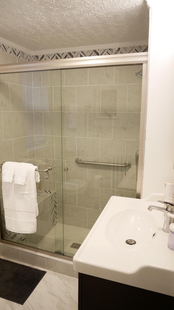 Ein Badezimmer mit Duschkabine aus Glas, einem weißen Waschbecken und einer schwarzen Badmatte.