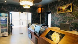 Interior de una cafetería con mostrador de madera, una computadora portátil, un refrigerador y un letrero que dice "The 50 Coffee Shop".