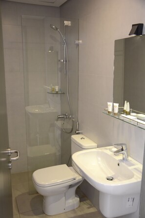 Une salle de bain moderne avec une douche à parois de verre, des toilettes blanches et un lavabo avec un miroir au-dessus.