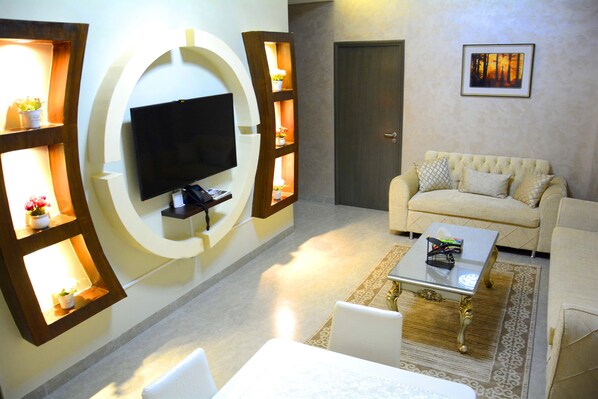 A living room with a flat-screen TV mounted on a wall, a beige sofa, a coffee table, and a patterned rug.