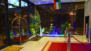 Un vestíbulo con alfombra roja, un carrito dorado, plantas en macetas y una barrera de cuerda roja.