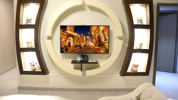 Una sala de estar moderna con un televisor de pantalla plana montado en una pared circular, rodeada de estantes de madera con plantas en macetas.