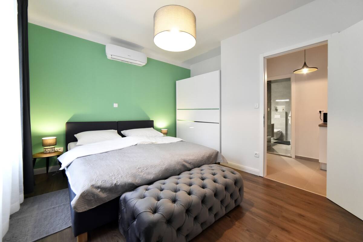 Ein modernes Schlafzimmer mit Bett, Bank und grünen Wänden.