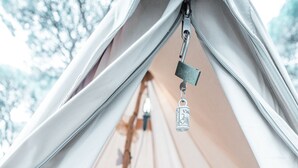A tent interior with a bed, a small table, and a hanging plant. - Pigna Felice - Glamping (Grosseto)