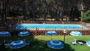 A swimming pool with a wooden deck, surrounded by trees. There are lounge chairs and umbrellas. - Pigna Felice - Glamping (Grosseto)