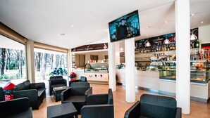 A modern bar area with wicker furniture, a television screen, and a variety of beverages and snacks. - Pigna Felice - Glamping (Grosseto)
