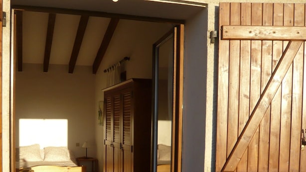 A bedroom with a bed, wooden wardrobe, and a large wooden door.