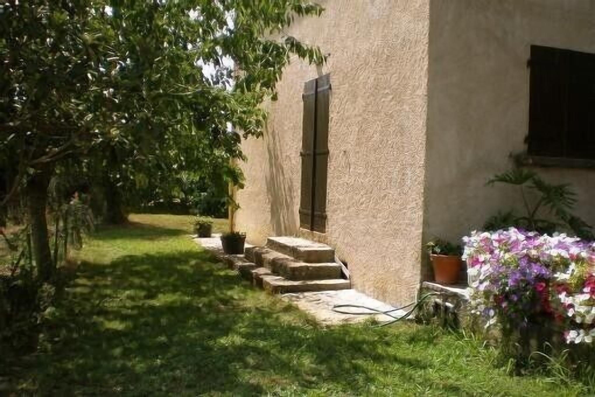 A building with a stone facade, a set of stone steps leading to a door, and a garden area with potted plants and a flower arrangement.