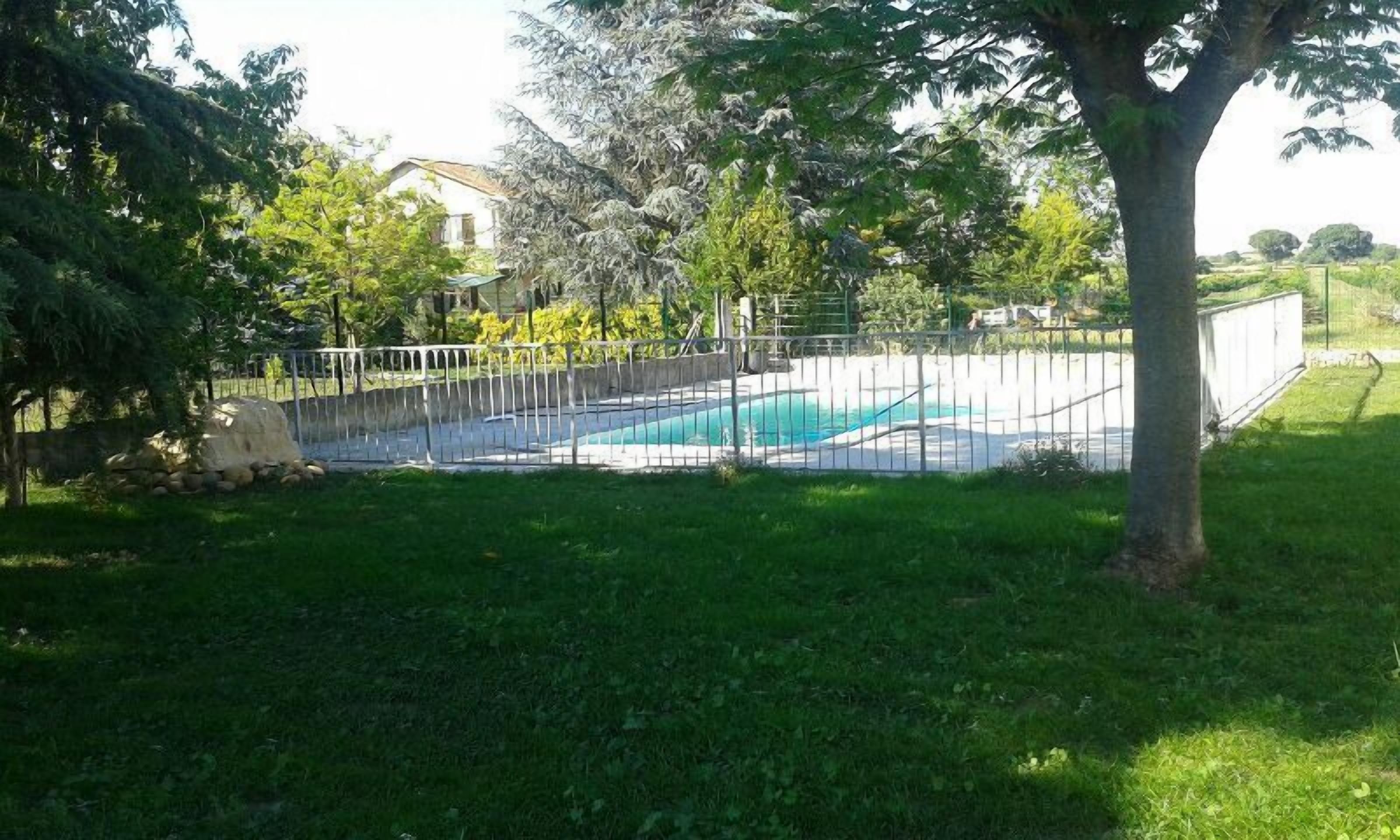 A swimming pool surrounded by a fence, with a grassy area and trees in the background.