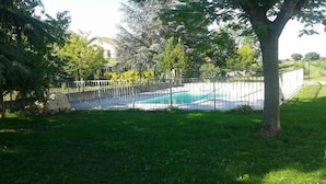 A swimming pool surrounded by a fence, with a grassy area and trees in the background.