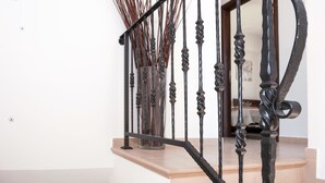 A staircase with a black wrought iron railing, a vase with tall, thin plants, and a butterfly decoration on the wall. - Natalie Villa CL 41 (Paralimni)