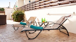 A patio with two lounge chairs, a table with bottles, and a wooden wall. - Natalie Villa CL 41 (Paralimni)